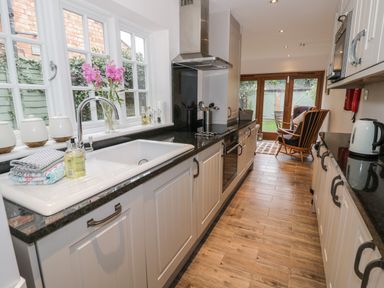A kitchen with a sink countertop oven wooden cabinets and a chair near glass doors at 24 College Lane Stratford-Upon-Avon