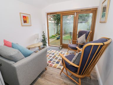 A small sitting area with two wooden frame armchairs and a gray sofa near sliding glass doors opening to a garden at 24 College Lane in Stratford-Upon-Avon