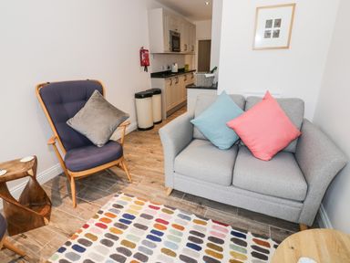 A living room with a gray sofa with blue and pink cushions a wooden side table a purple armchair and a colorful rug at 24 College Lane in Stratford-Upon-Avon