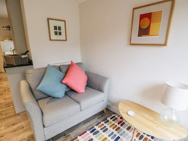 A small living area with a grey sofa with blue and red cushions a wooden table with a lamp and a patterned rug at 24 College Lane in Stratford-Upon-Avon