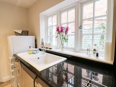 A kitchen sink with soap and towels next to a window with flowers and condiments at 24 College Lane in Stratford-Upon-Avon