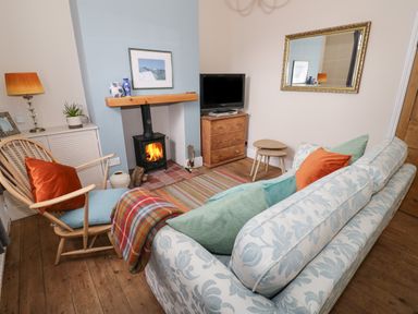 A living room with a wood stove fireplace a chair a patterned sofa with cushions a wooden chest of drawers and a large wall mirror at 24 College Lane in Stratford-Upon-Avon
