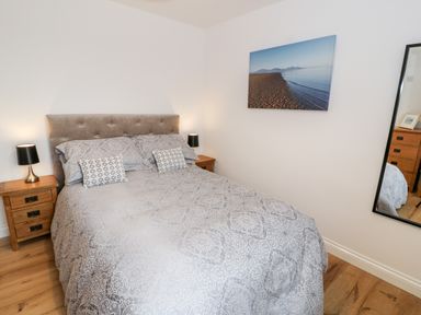 A bedroom with a double bed two wooden bedside tables with lamps a large wall mirror and a beach landscape picture at Ty'n Lon Bach in Llandwrog