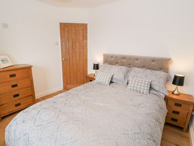 A bedroom with a double bed with patterned bedding two bedside tables with lamps and a wooden chest of drawers at Ty'n Lon Bach in Llandwrog