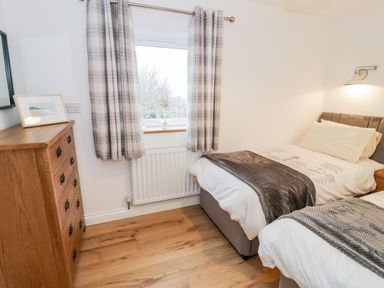 A bedroom with two single beds a wooden chest of drawers and a window with plaid curtains at Ty'n Lon Bach in Llandwrog