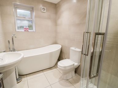 A bathroom with a bathtub, toilet, sink, shower enclosure, and a window at Ty'n Lon Bach in Llandwrog