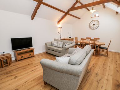 A living room with two sofas a wooden dining table with chairs a television on a stand and wooden ceiling beams at Ty'n Lon Bach in Llandwrog