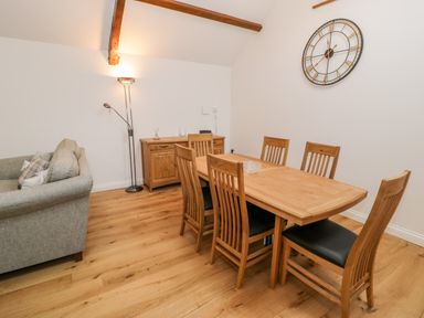 A dining area with a wooden table and six chairs next to a grey sofa and wooden sideboard at Ty'n Lon Bach in Llandwrog