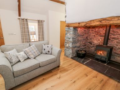 A living room with a gray sofa with cushions a stone fireplace with a wood burning stove and wooden floor at Ty'n Lon Bach in Llandwrog
