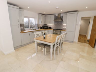 A kitchen with a wooden dining table and four chairs a stove a microwave and cupboards at Ty'n Lon Bach in Llandwrog