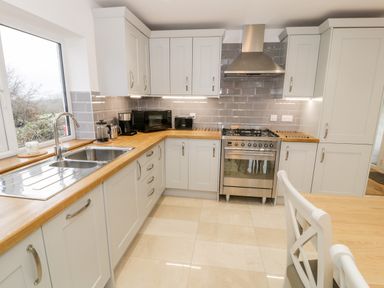A kitchen with white cabinets wooden countertops a stainless steel sink a gas stove microwave and a chair at Ty'n Lon Bach in Llandwrog
