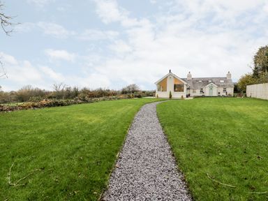 A gravel path leading through a green lawn to a white house with a green door at Ty'n Lon Bach in Llandwrog