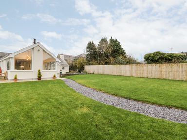 A backyard with green grass gravel path wooden fence and part of a house with large windows at Ty'n Lon Bach in Llandwrog