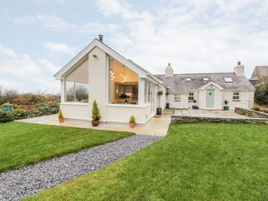A house with a glass extension and green lawn in the foreground at Ty'n Lon Bach in Llandwrog