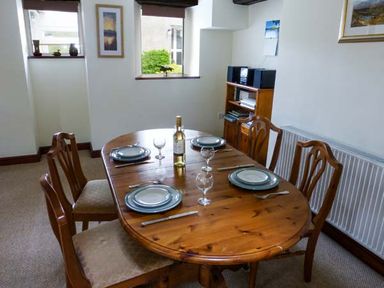 A dining room with a wooden table set for four with plates and glasses at Kingfisher Barn in Staveley near Windermere