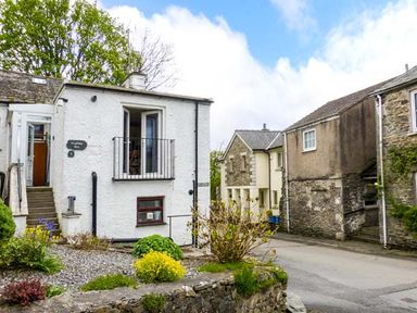 White building with an upper balcony and garden bordered by stone walls on a street with stone houses at Kingfisher Barn in Staveley near Windermere