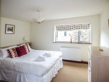 A bedroom with a double bed with three decorative pillows and folded towels a chest of drawers and a window with a floral blind at Kingfisher Barn in Staveley near Windermere