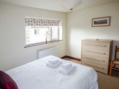 A bedroom with a bed holding folded white towels near a window a chest of drawers and a chair at Kingfisher Barn in Staveley near Windermere