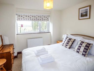 A bedroom with a double bed two patterned pillows wooden dresser and a window with patterned blinds at Kingfisher Barn in Staveley near Windermere