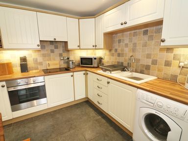 A kitchen with white cabinets wooden countertops a stove microwave toaster sink and washing machine at Kingfisher Barn in Staveley near Windermere
