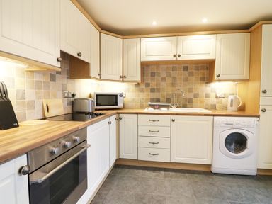 A kitchen with wooden countertops white cabinets tiled backsplash stove oven microwave toaster sink kettle and washing machine at Kingfisher Barn in Staveley near Windermere