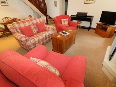 A living room with red and plaid sofas a wooden coffee table a television and a digital piano at Kingfisher Barn in Staveley near Windermere