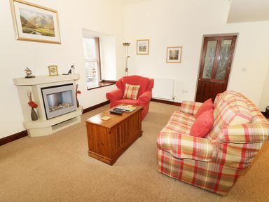 A living room with a plaid sofa and red armchair near a wooden chest and fireplace at Kingfisher Barn in Staveley near Windermere
