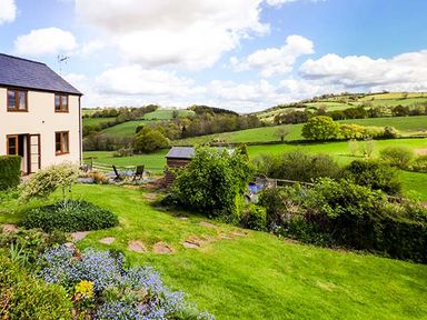 A garden with flowers and shrubs next to a house overlooking green fields and hills at Glebe Farm Cottage in Llandegveth near Cwmbran