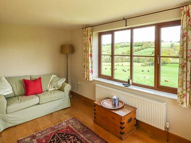 A living room with a sofa a floor lamp a wooden chest a window with curtains and a view of green fields at Glebe Farm Cottage in Llandegveth near Cwmbran