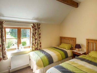 A bedroom with two single beds and a window with floral curtains at Glebe Farm Cottage in Llandegveth near Cwmbran