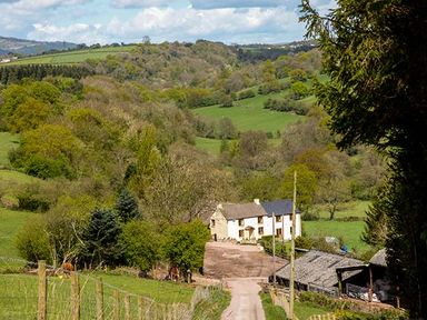 A country house at the end of a dirt road surrounded by trees and hills at Glebe Farm Cottage in Llandegveth near Cwmbran