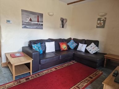 A living room with a black sectional sofa with multiple decorated cushions and wooden side tables at Kingfisher Cottage in Llanboidy
