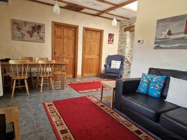 A living room with a black sofa with cushions a wooden dining table with chairs two wooden doors and a blue armchair at Kingfisher Cottage in Llanboidy