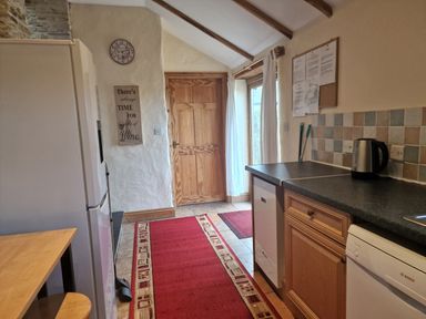 A kitchen with wooden door red rugs refrigerator kettle and dishwasher at Kingfisher Cottage in Llanboidy
