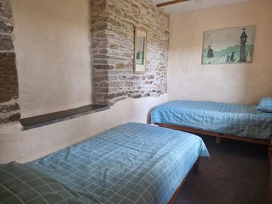 A bedroom with two single beds with blue checkered bedspreads and exposed stone walls at Kingfisher Cottage in Llanboidy