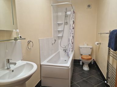 A bathroom with a sink a bathtub with shower and a toilet with wooden seat at Kingfisher Cottage in Llanboidy