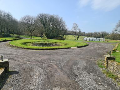 A gravel driveway with a roundabout and pond surrounded by grass and trees in a countryside setting at Kingfisher Cottage in Llanboidy