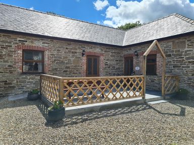An outdoor patio with wooden railing and stone walls under a blue sky at Swallow Cottage in Llanboidy
