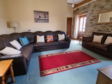 A living room with two brown leather sofas a red rug and a stone wall at Swallow Cottage in Llanboidy