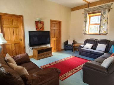 A living room with brown leather sofas a red rug a wooden TV stand a flat screen TV and two wooden doors at Swallow Cottage in Llanboidy