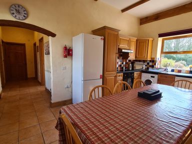 A kitchen with wooden cabinets a white refrigerator a tiled floor a dining table with checked tablecloth and wooden chairs at Swallow Cottage in Llanboidy