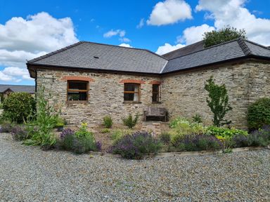 A stone cottage with three windows and a slate roof with plants and gravel in front at Swallow Cottage in Llanboidy