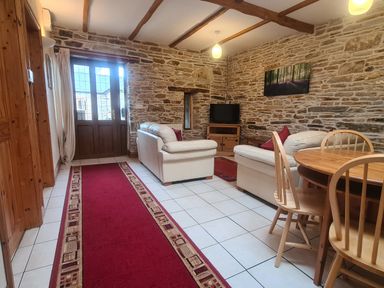 A living room with stone walls wooden beams white tile floor white sofas wooden dining table and chairs at Sandpiper Cottage in Llanboidy