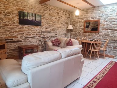 A living room with cream sofas red cushions a wooden dining table and chairs with stone walls at Sandpiper Cottage in Llanboidy