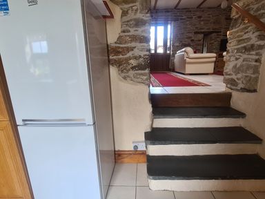 Stone steps leading to a living room with a red rug beige sofa and wooden door next to a white fridge in a stone wall house at Sandpiper Cottage in Llanboidy