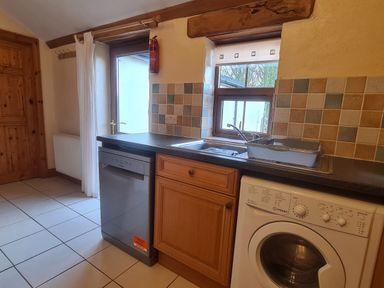 A kitchen with dishwasher washing machine sink and wooden cabinets at Sandpiper Cottage in Llanboidy