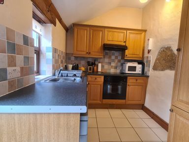 A kitchen with wooden cabinets a black oven microwave and a sink at Sandpiper Cottage in Llanboidy