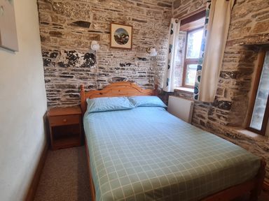 A bedroom with a bed a bedside table and windows with curtains at Sandpiper Cottage in Llanboidy