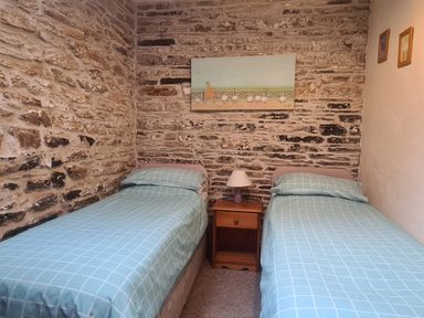 A bedroom with two single beds a wooden nightstand with a lamp a wall painting and stone walls at Sandpiper Cottage in Llanboidy