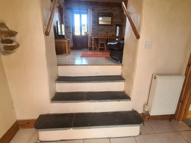 Three stone steps leading to a room with dining table chairs a television and a brown sofa at Puffin Cottage in Llanboidy
